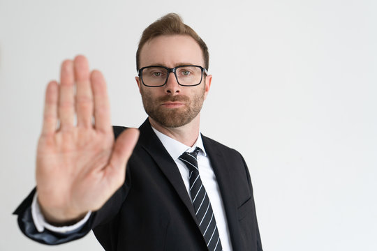 Serious business man showing open palm or stop gesture and looking at camera. Restriction concept. Isolated front view on white background.