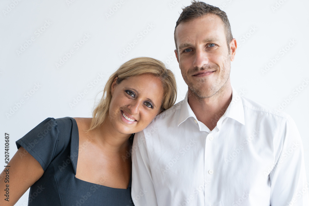 Wall mural Portrait of happy mid adult couple looking at camera and smiling. Blond-haired wife leaning her head on shoulder of husband. Happy couple concept