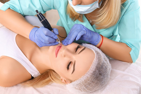 Cosmetologist making permanent makeup on woman's lips