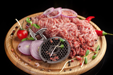 Raw chopped meat. Knife and grill from meat grinder, olive oil, spices, cherry, chili pepper, black pepper lie on a wooden board. Ready for cooking.