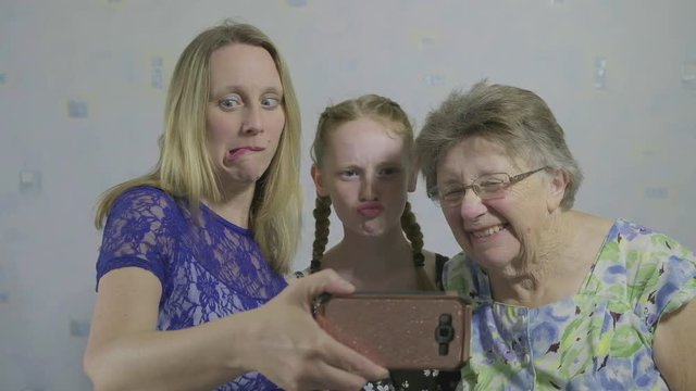 Three generations of the same family taking a selfie on a smartphone pulling funny faces