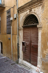 The old arch wooden door in the yellow stone house on the small pedestrianized paved street on the sunny day.