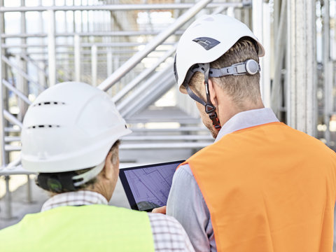 Architect and foreman with tablet wearing hard hat on construction site