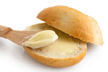 Gordijnen Detail of butter spread on a cut crusty bread roll with a wooden knife isolated on white. © Moving Moment