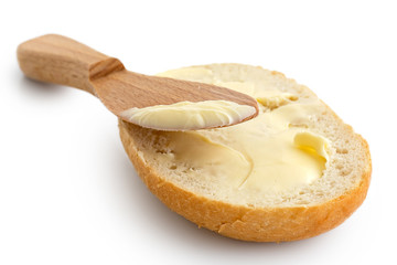 Fototapeta na wymiar Butter spread on a half of crusty bread roll with a wooden knife isolated on white.