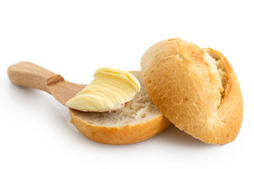 Butter on wooden knife resting on a cut crusty bread roll isolated on white.