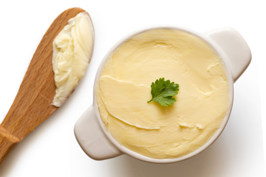 Round Ceramic Dish Filled With Butter Next To A Wooden Knife On White Background From Above. Parsley Garnish.