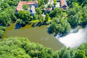 The pond at the moated castle Neuhaus from the air, with bushes and trees, at the edge of the village