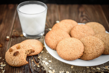 Homemade oatmeal cookies with raisins, cinnamon with milk on dark wooden background.