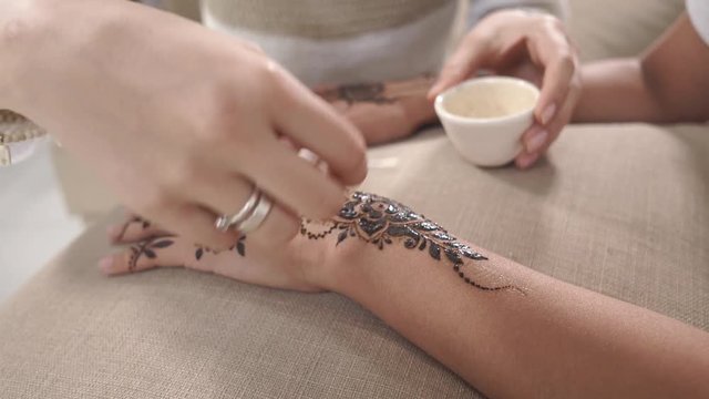 close up shot of a woman who works at the spa salon as a make-up artist, she applies a protective oil on a mehendie that was painted with henna