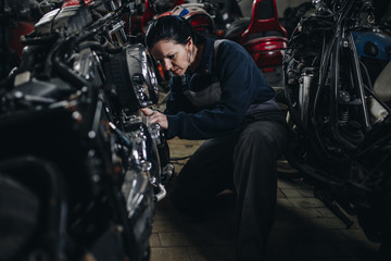 Obraz na płótnie Canvas Strong and worthy woman doing hard job in car and motorcycle repair shop.