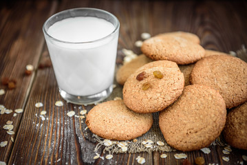 Homemade oatmeal cookies with raisins, cinnamon with milk on dark wooden background.
