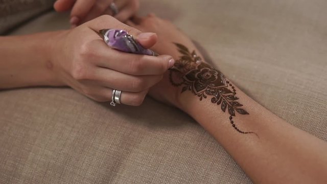 close up shot of the master hands, who uses a small tube of natural henna for a mehendi pattern, the master puts on the hand floral patterns