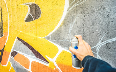 Detail of street artist painting colorful graffiti on public wall - Modern art concept with urban guy drawing live murales with multi color aerosol spray - Vintage filter with focus on yellow paint