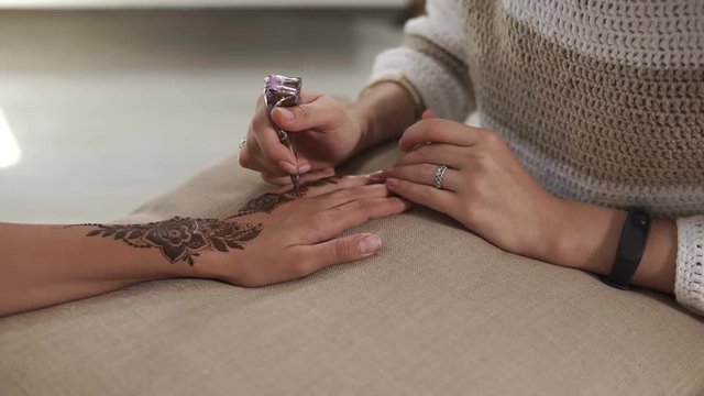 close up shot of the woman's hands, on a thin tanned hand put a neat and beautiful floral henna tattoo, the visitor of the spa salon will be pleased