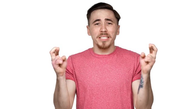 Portrait of superstitious european man wearing casual t-shirt begging with fingers crossed and screaming god please, isolated over white background. Concept of emotions