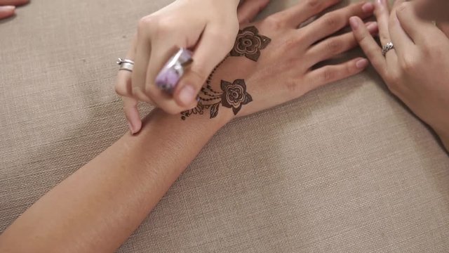 close up shot of a woman's hands, the lady is waiting for the completion of the mehendi on the wrist and fingers of her hands, the master finishes drawing tattoos with henna