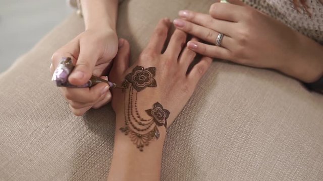 Close up shot of a woman connecting henna flowers on a hand. Woman is using henna cone for drawings. Dying hands skin.