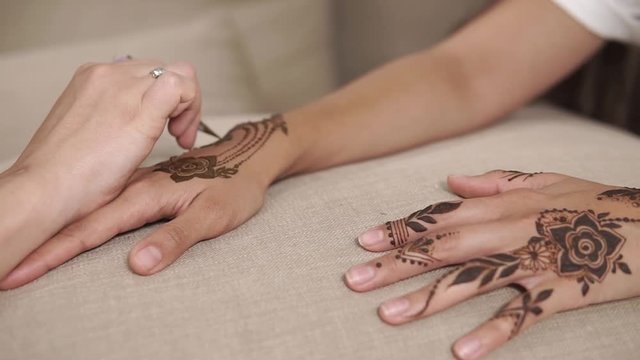 close up shot of a woman's hands, who makes mehendi at home with a friend, the lady is engaged in decorating her skin, maybe she is preparing for a traditional gala event