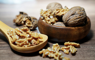 Whole walnuts and kernel walnuts in wooden bowl and wooden spoon on dark walnut table background.