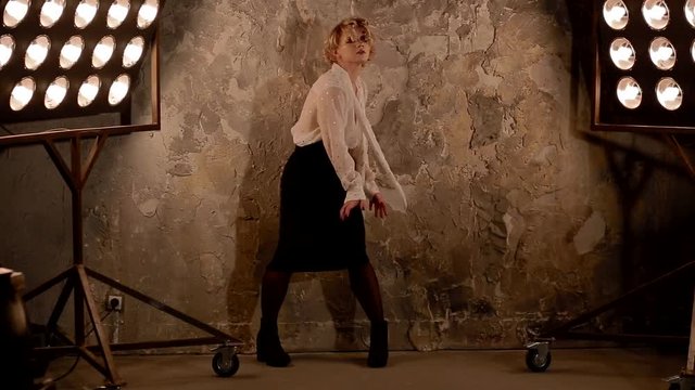 Young female blonde caucasian dancer dancing in front of studio light. Overall plan.