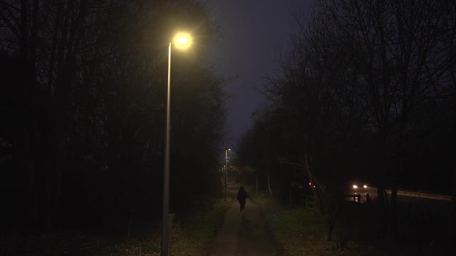 Hooded figure running down a path at night