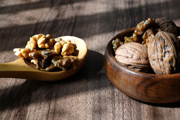 Whole walnuts and kernel walnuts in wooden bowl and wooden spoon on dark walnut table background.