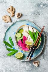 Vegan asian udon noodles soup bowl with ginger and mushrooms broth, tofu, snap peas, zucchini, watermelon radish and lime.