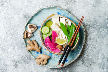 Vegan asian udon noodles soup bowl with ginger and mushrooms broth, tofu, snap peas, zucchini,...