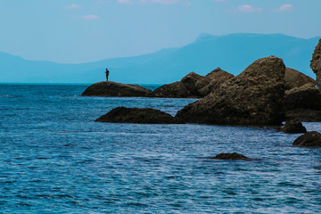Beautiful scenery in the evening at the Sea. A man standing far away on the cliff near smooth sea.
