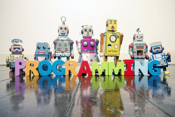 the word  PROGRAMMING with wooden letters and retro toy robots  on an old wooden floor