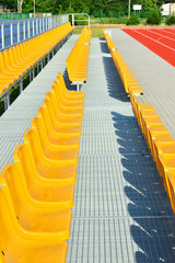 Żółte plastikowe krzesełka na trybunie stadionu sportowego.