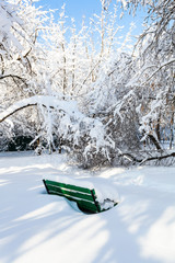 green bench in snow-covered urban garden in winter