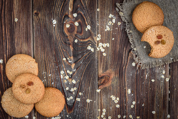 Homemade oatmeal cookies with raisins, cinnamon with milk on dark wooden background.