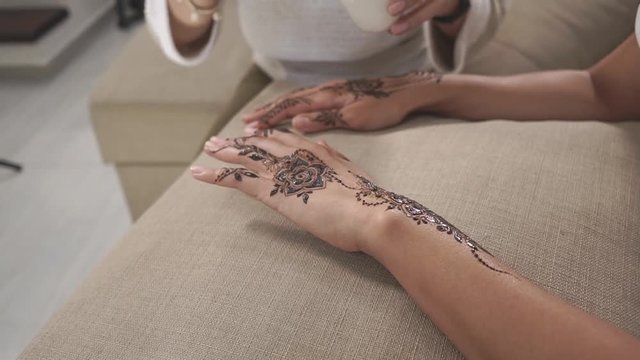 Woman is applying natural oil on henna ornament on female hands. Moisturizing for extending lifetime of stain on skin, traditional eastern body art