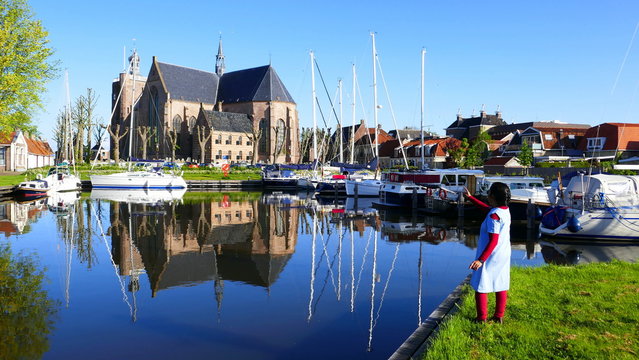 junge Frau am Hafen von Workum beobachtet Spiegelung der Kirche und der Schiffe im Wasser