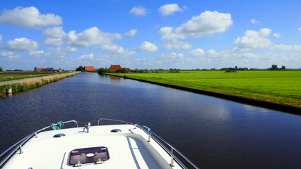 Hausboot fährt  auf ruhigem Kanal durch die flache Landschaft in Friesland an sonnigem Tag