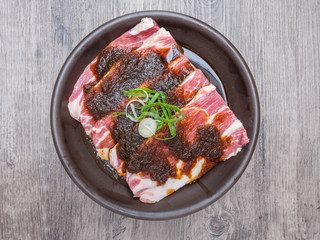 Slice raw pork with marinate in ceramic plate on wood background