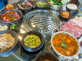 Table of set of korean barbecue, pork, meat, rice, vegetables, sauce and hood