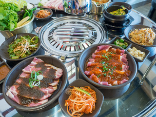 Table of set of korean barbecue, pork, meat, rice, vegetables, sauce and hood