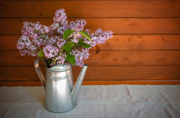 Watering can with branches of lilac flower