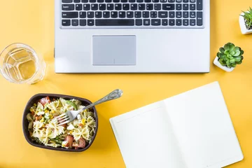  Groentesalade met macaroni-kommen met kaas in een container voor de lunch op de kantoorwerkplek in de buurt van de laptop. Bovenaanzicht, plat gelegd © svitlini