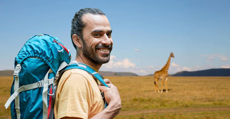 adventure, travel, tourism, hike and people concept - smiling man with backpack over giraffe in african savannah background