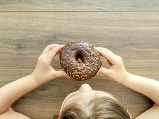 Child eating a donut on wooden background with copy space. Unhealthy eating concept, top view