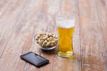 food and drinks concept - glass of draught beer, smartphone and pistachio nuts on table
