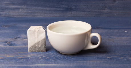Tea time concept. Cup or white porcelain mug with transparent hot water and bag of tea. Process of tea brewing in ceramic mug. Mug filled with boiling water and teabag on blue wooden background