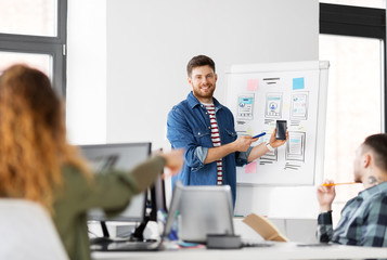 business, technology and people concept - man showing smartphone user interface design to creative team at office presentation