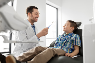 Obraz premium medicine, dentistry and healthcare concept - male dentist showing toothbrush to kid patient at dental clinic
