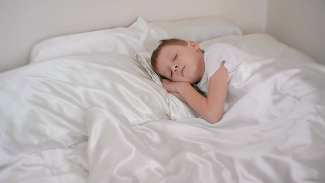 Seven-year-old a boy quietly sleeping in bed in his room, putting hands under his head.