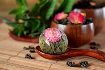 Blossom tea ball and leaf tea with rose petals in wooden cups and spoon